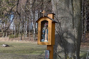 Pod stromy je maličká kaplička (IČ)